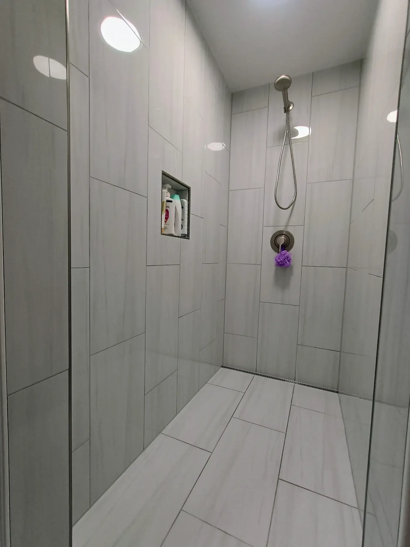 Shower interior with large gray tile walls, built-in niche and hand shower