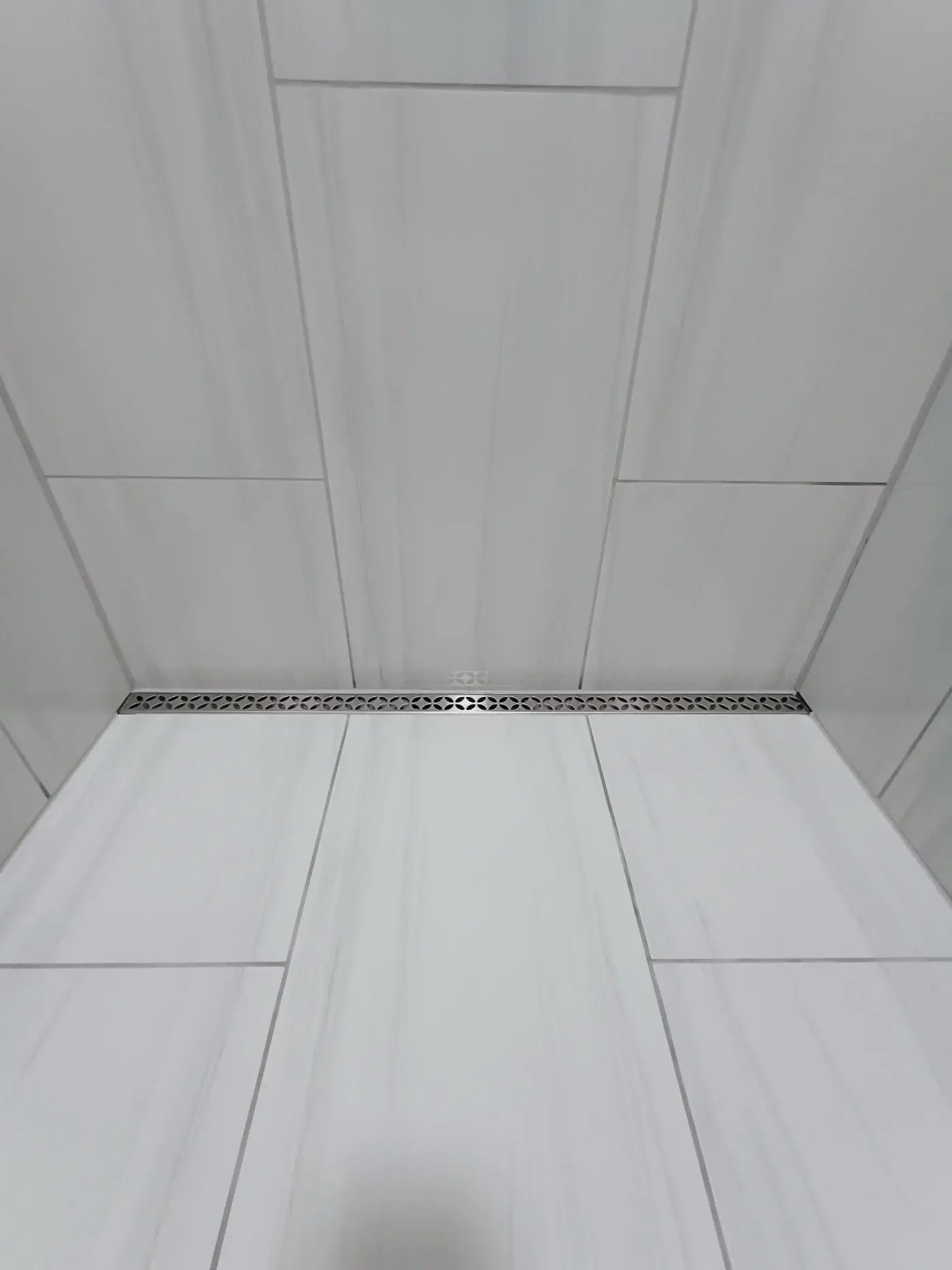 Shower floor detail showing decorative linear drain with large format tile