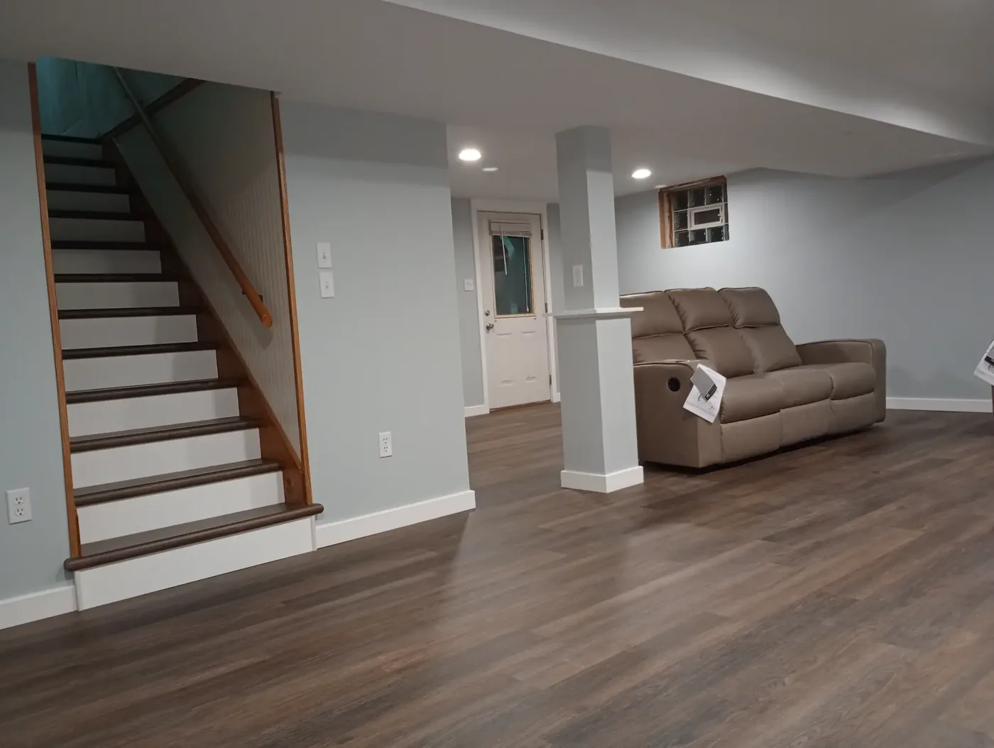 Finished basement open living area with LVP flooring, recessed lighting and white staircase