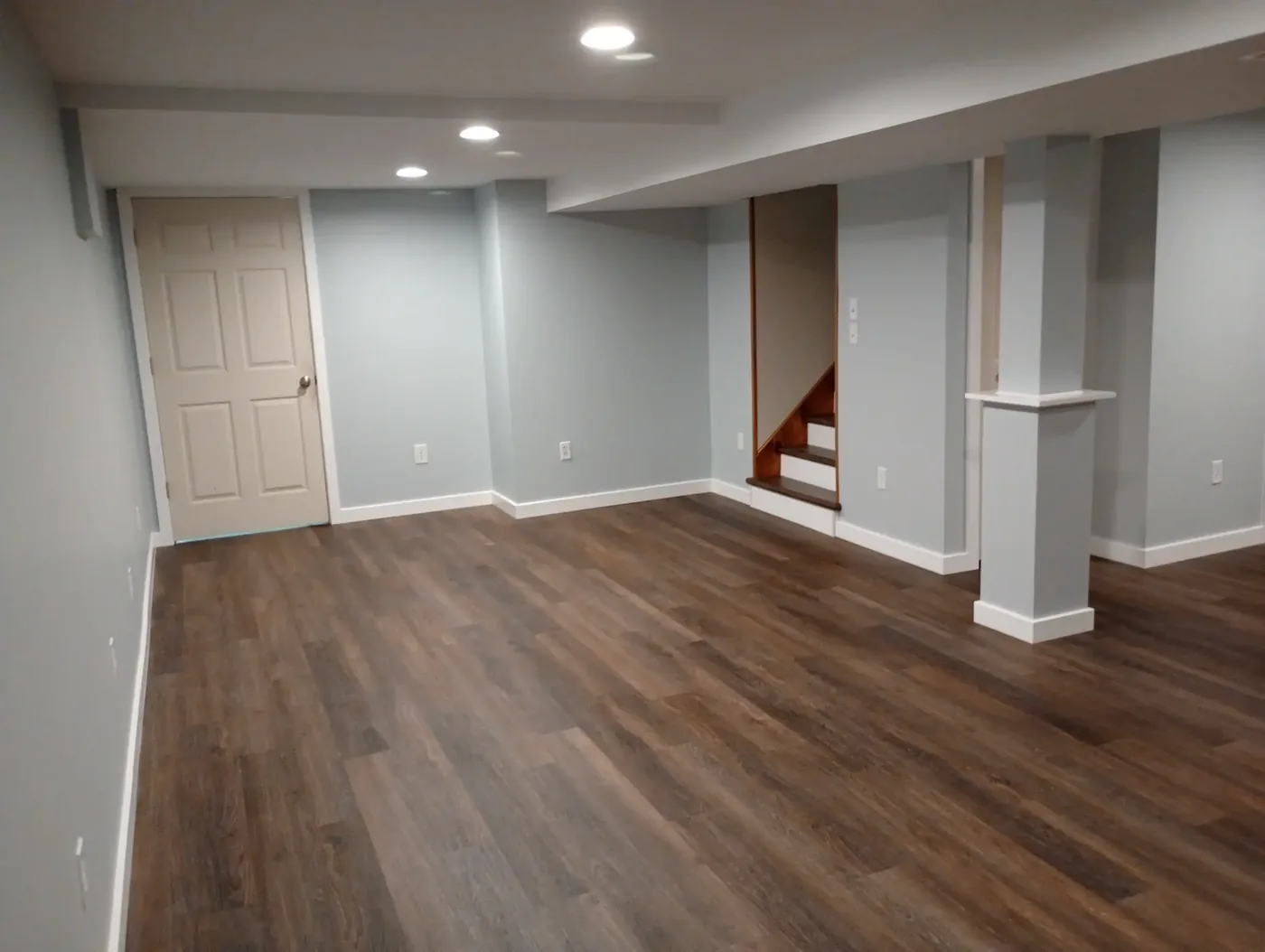 Finished basement with dark LVP flooring, white support columns and recessed lighting